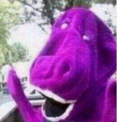 a purple dog with its mouth open and hands up in the air, wearing a green shirt