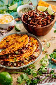 some tacos are sitting on a table next to bowls of chili and limes