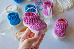 a hand holding a small crocheted baby booties next to yarn and scissors