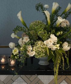 a vase filled with white flowers sitting on top of a black table next to candles