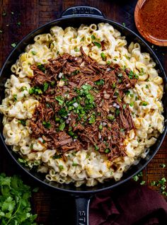 a skillet filled with pasta and meat on top of a wooden table next to some parsley