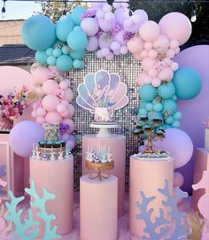 a table topped with lots of pink and blue desserts next to giant balloons in the shape of sea animals