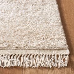 a white rug with fringes on top of a wooden floor next to a wood floor