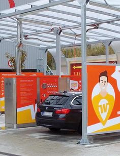 a car is parked in front of an orange and white bus stop with advertisements on it