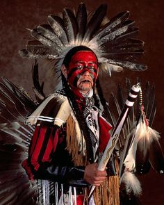 a native american man dressed in red, white and black with feathers on his head