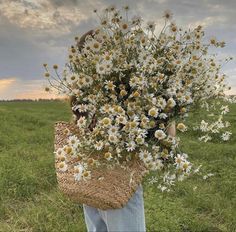 a person standing in a field holding a basket full of daisies