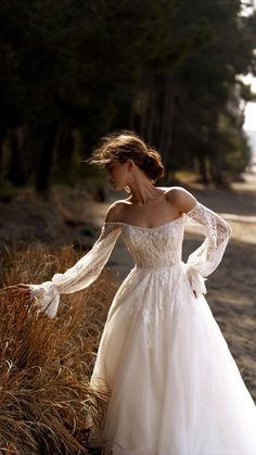 a woman in a wedding dress is standing on the beach with her arms out and looking down