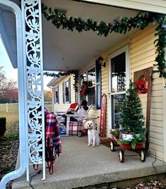 a dog sitting on the front porch of a house with christmas decorations and presents around it