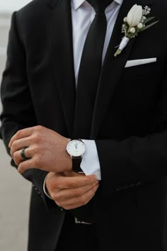 a man in a black suit and white flower boutonniere on his wrist