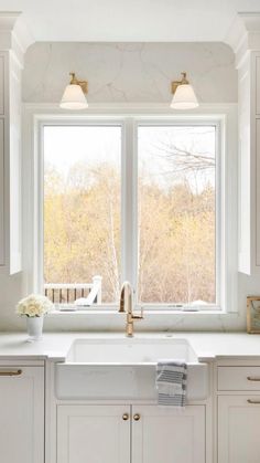 a kitchen with white cabinets and marble counter tops is pictured in this image, there are two windows above the sink