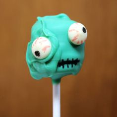 there is a green cake on a stick with eyes and mouthballs painted on it