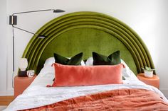 a bed with green headboard and two orange pillows on it's sides, in front of a white wall