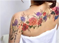 the back of a woman's shoulder with flowers and words tattooed on her arm