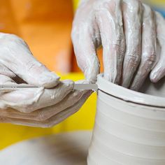 a person with white paint on their hands is using a knife to decorate a vase