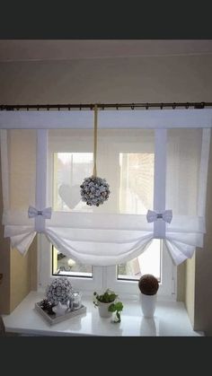 the window is decorated with white curtains and flowers in vases on top of a table