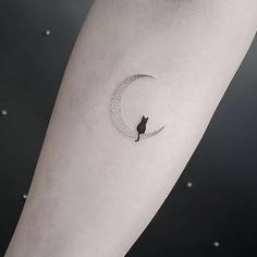 a cat sitting on the moon tattoo on the left inner arm, with stars in the background