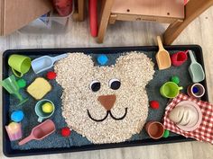 a child's play mat with a bear face made out of sand and plastic cups