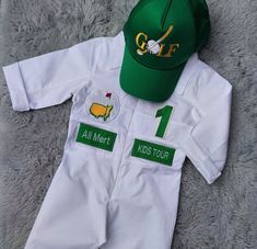 a green and white golf outfit with a hat on the top is laying on a gray carpet