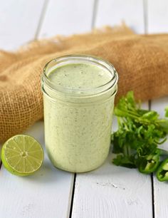 a green smoothie in a mason jar with a lime slice next to it on a white wooden table