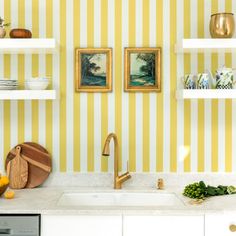 a kitchen with yellow and white striped wallpaper, two pictures on shelves above the sink