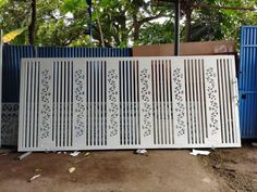 two white gates with designs on them in front of a blue fence and some trees