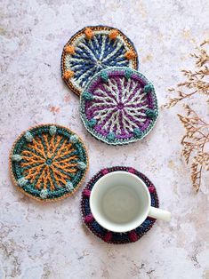 three crocheted coasters sitting on top of a table next to a cup