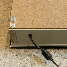 a cord is plugged into the side of a metal box on carpeted floor