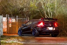 the back end of a black car parked in front of a fenced off area