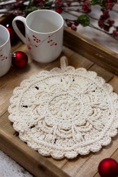 a crocheted doily sits on a wooden tray next to two mugs