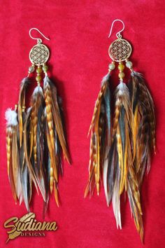 two pairs of earrings with feathers hanging from them on a red cloth covered tablecloth