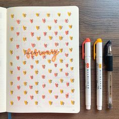 an open notebook with writing on it next to two markers and a pen, which are sitting on top of a wooden table