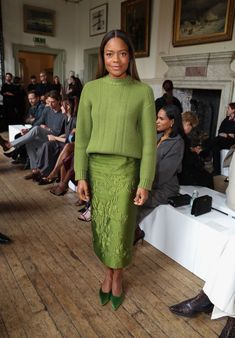 a woman standing in front of a group of people wearing green dresses and heels on the runway