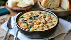 there is a bowl of soup with meat and vegetables in it next to bread on the table