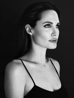 a black and white photo of a woman with long hair wearing a bra looking at the camera