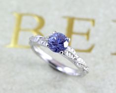 a tan and white gold engagement ring with a blue sapphire in the center, on top of a beige background