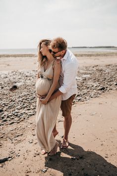 a pregnant couple kissing on the beach