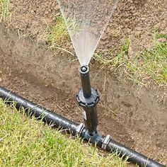 a sprinkler is spraying water onto the ground next to a black pipe