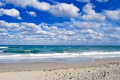 an empty beach with waves coming in to the shore and blue sky filled with clouds