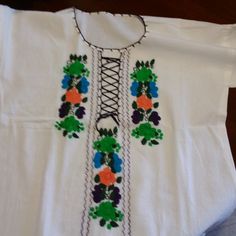 a white t - shirt with colorful flowers and lace on the neckline is laying on a wooden surface