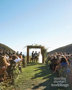 a wedding ceremony on the side of a hill with people sitting in chairs and looking at each other