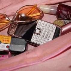 an assortment of items that include sunglasses, lipstick, cell phone and pill bottle sitting on a pink blanket