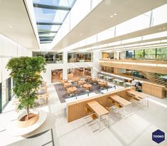 the interior of an office building with many tables and chairs, trees in the center