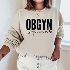 "The \"OBGYN Squad Sweatshirt\" is a sturdy and warm sweatshirt bound to keep you warm in the colder months. Perfect gift for a birthday or the holidays! A pre-shrunk, classic fit sweater that's made with air-jet spun yarn for a soft feel and reduced pilling. Sweatshirt details: * 50% cotton, 50% polyester * Pre-shrunk * Classic fit with no center crease * 1x1 athletic rib knit collar with spandex * Air-jet spun yarn with a soft feel and reduced pilling * Double-needle stitched collar, shoulders Nana Sweater, Gigi Gifts, Gigi Gift, Custom Crewneck Sweatshirts, Grandma Sweatshirt, Baseball Sweatshirts, Gifts For Grandma, Gift For Grandma, Mama Sweatshirt