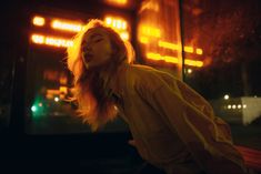 a woman standing in front of a building at night with her eyes closed and head turned to the side