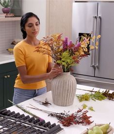 a woman arranging flowers in a vase on a kitchen counter