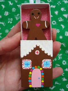 a hand holding a small cardboard house with a gingerbread man in the front door