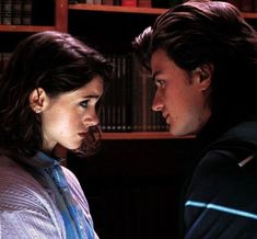 a young man and woman standing next to each other in front of bookshelves