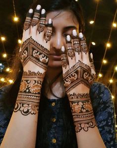 a woman holding her hands up to her face with henna tattoos on it's arms