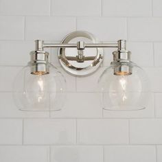 two light bathroom fixture with clear glass globes on the wall and white tiles in the background