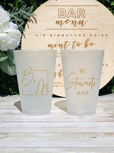 two shot glasses sitting next to each other on top of a wooden table with white flowers in the background